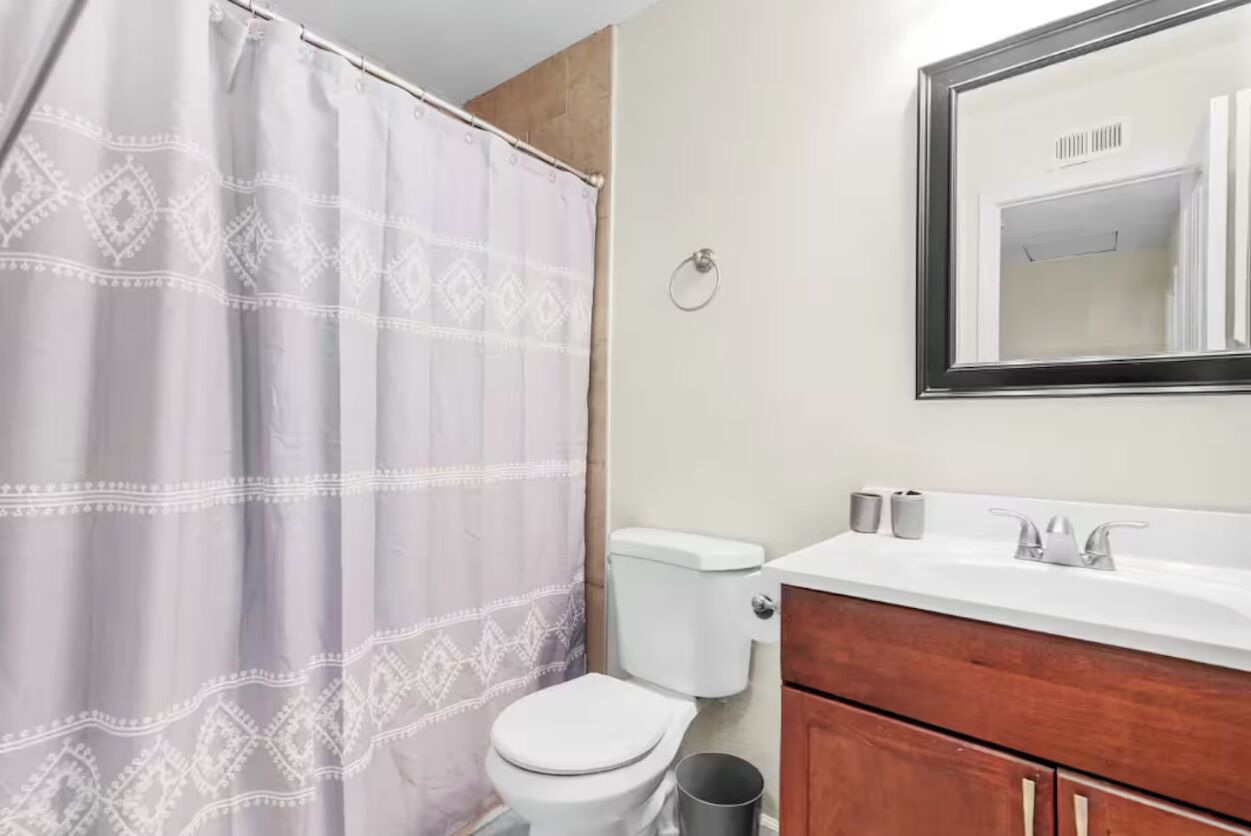 Een badkamer met douchegordijn, toilet, wastafel en spiegel.