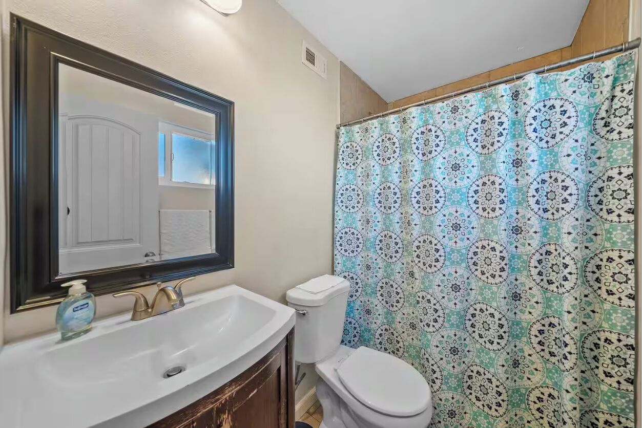 Een badkamer met een wit wastafel, een spiegel, een toilet en een douchegordijn met een geometrisch patroon.