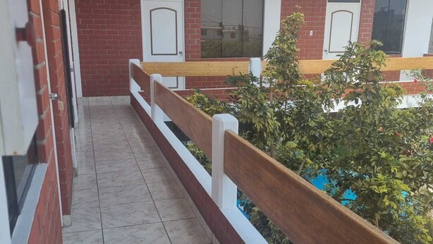 A corridor with a tiled floor, a wooden railing, and a view of a building with red brick walls and windows. - Hermosa casa en playa pulpos, cerca de las playas, comercial KM40 . (Punta Hermosa)