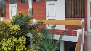 A multi-story building with red brick walls, white doors, and windows. There are balconies with wooden railings and a variety of plants in the foreground. - Hermosa casa en playa pulpos, cerca de las playas, comercial KM40 . (Punta Hermosa)
