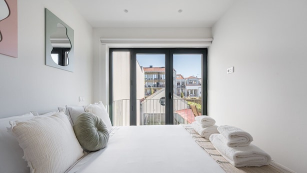 Quarto moderno com cama grande, varanda e vista para a cidade, além de cama arrumada com toalhas.
