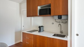 Cozinha compacta com armários de madeira, micro-ondas embutido, pia e máquina de café.