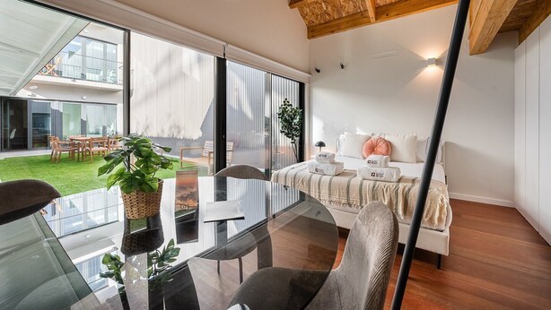 A modern interior with a glass dining table, a sofa, and a bed with towels. - GuestReady - Silk Factory - B (Porto)