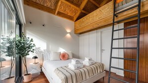 A bedroom with a wooden ceiling, a bed with white bedding and a striped throw, a ladder, and a potted plant by the window. - GuestReady - Silk Factory - B (Porto)