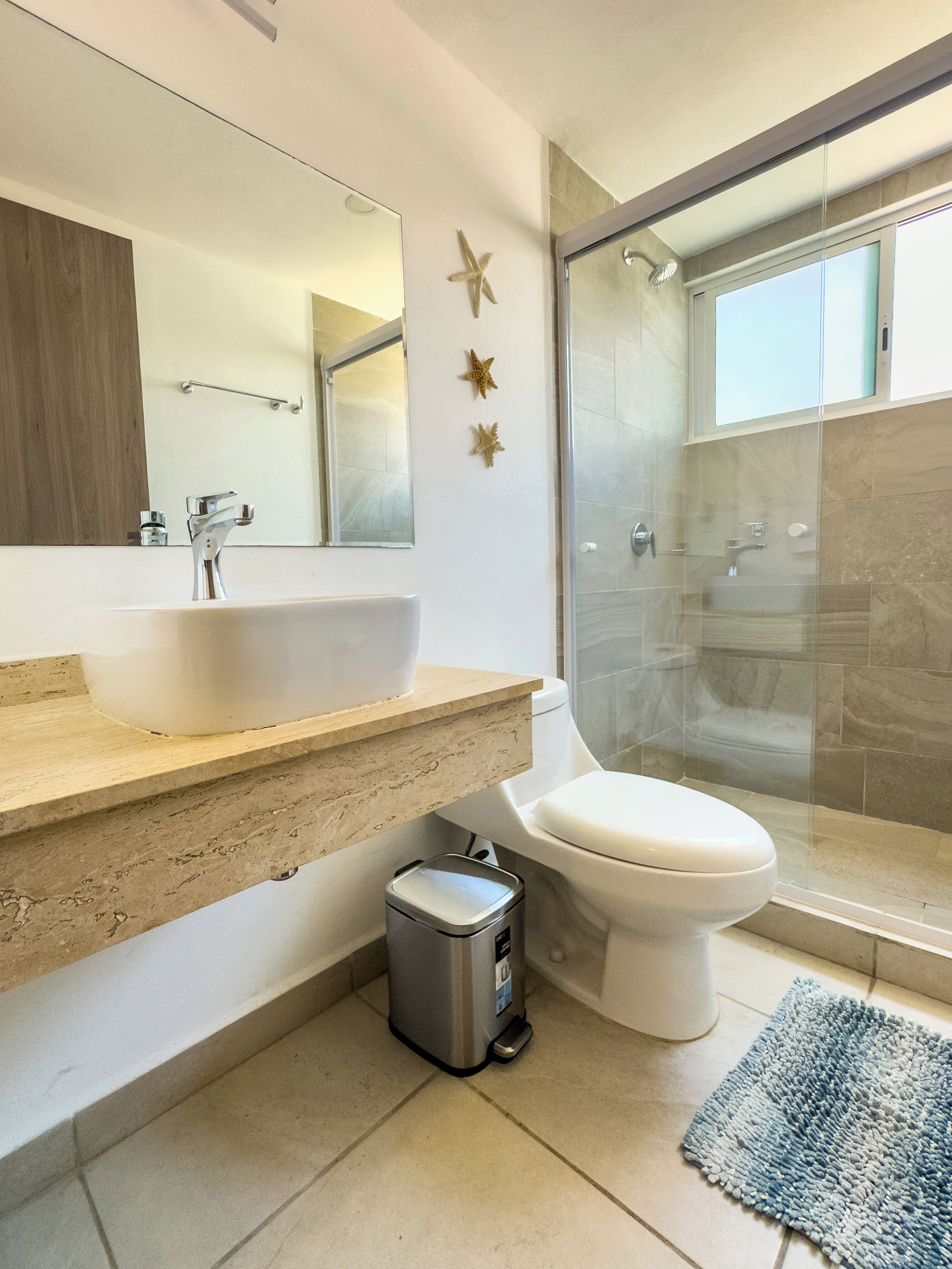 A modern bathroom with a large mirror, a sink, a toilet, and a glass-enclosed shower.
