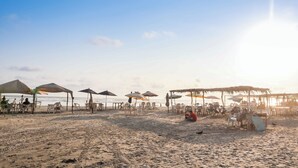 Una spiaggia con ombrelloni e lettini, una struttura in paglia e una distesa sabbiosa.