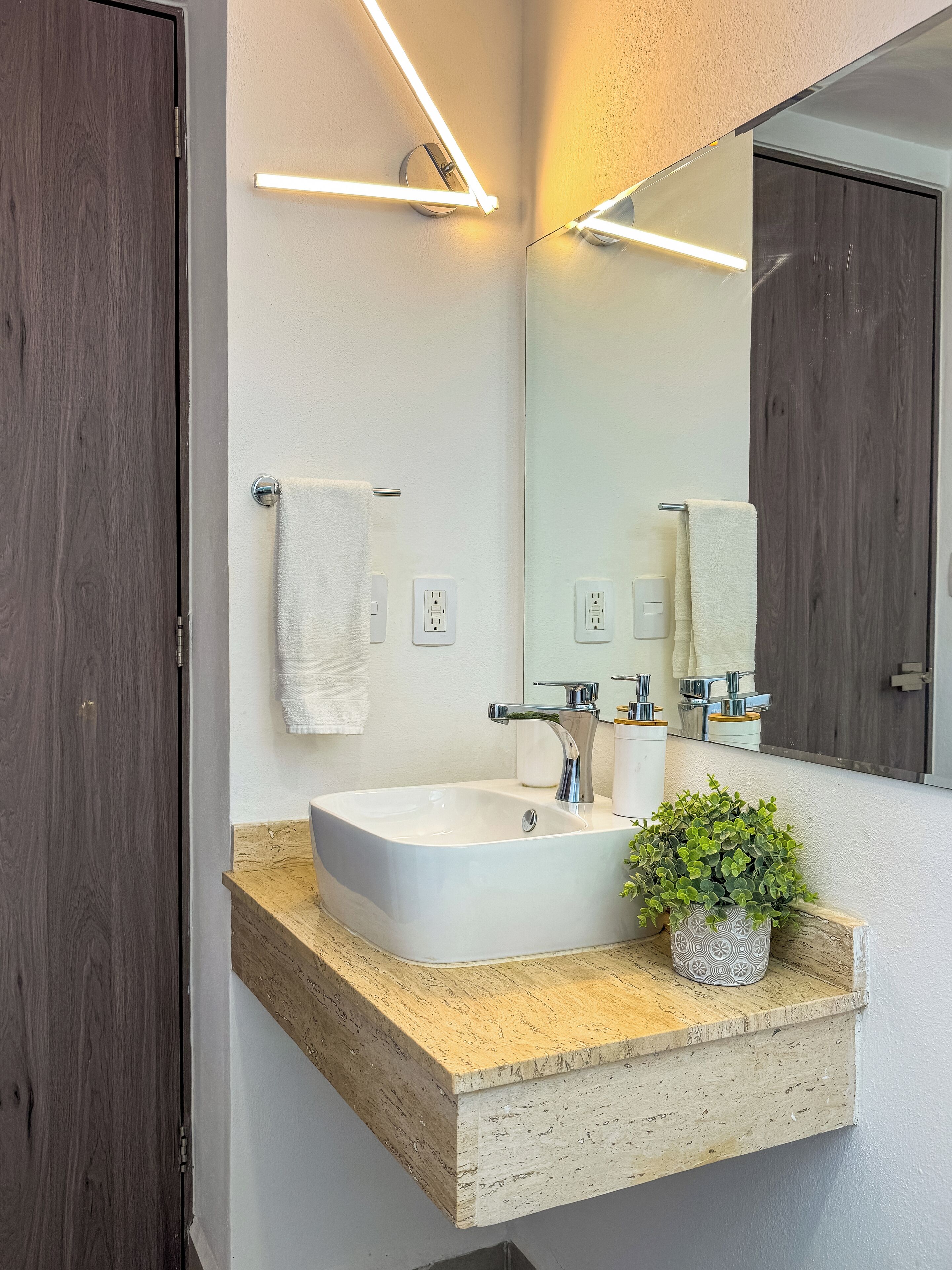 A modern bathroom with a large rectangular sink, a mirror, and a potted plant on the countertop.