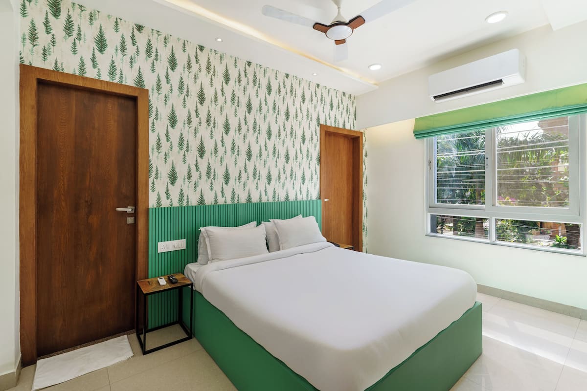 Une chambre à coucher avec un lit, une table de chevet, une porte en bois, une fenêtre donnant sur un paysage agréable et un ventilateur de plafond.