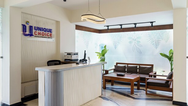 Zona de recepción de un hotel con un mostrador, un sofá y una mesita de centro. Un cartel en la pared dice 'Unique Choice Hotels Private Limited'.