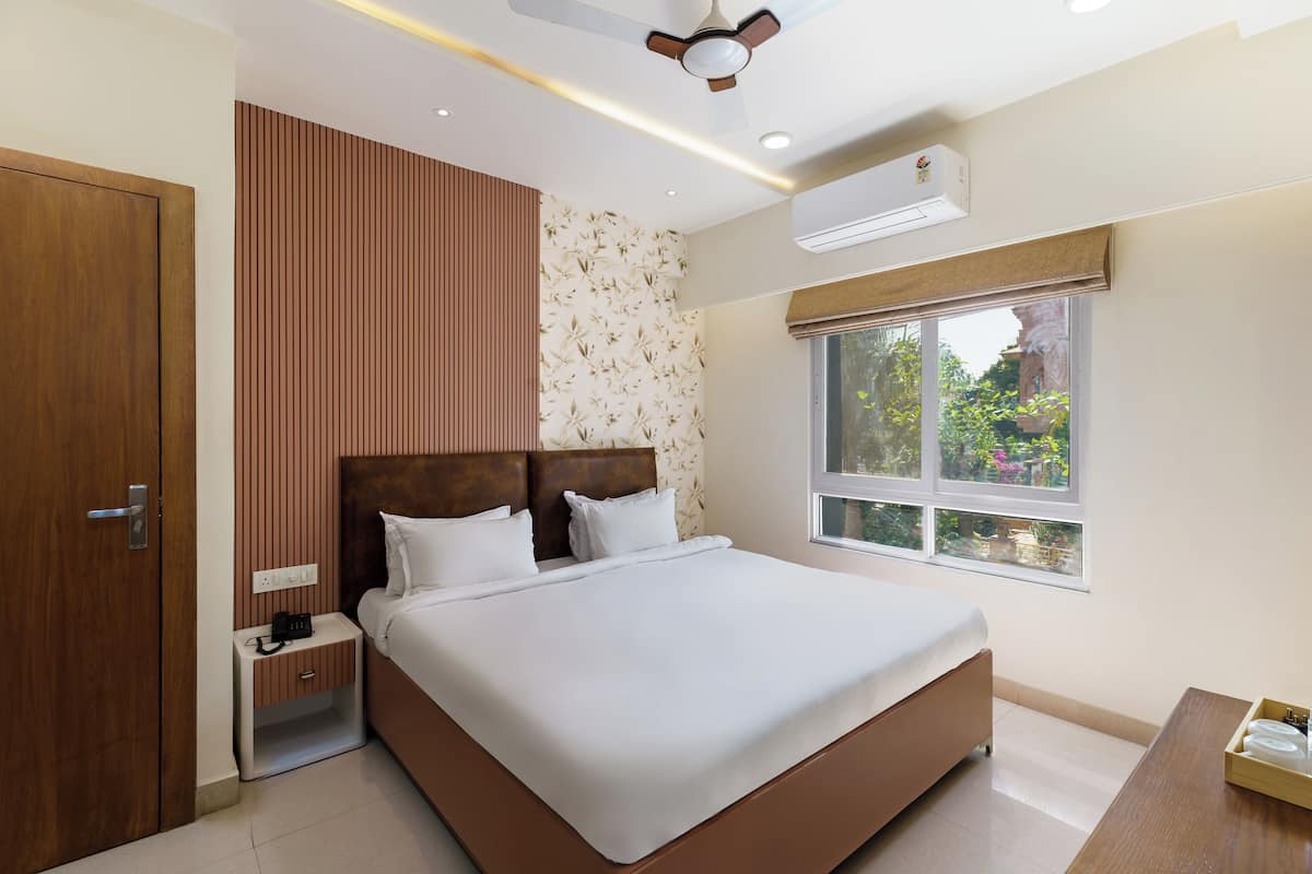 Une chambre moderne avec un grand lit, une armoire en bois, une table de chevet avec un téléphone et une fenêtre donnant sur un paysage verdoyant.