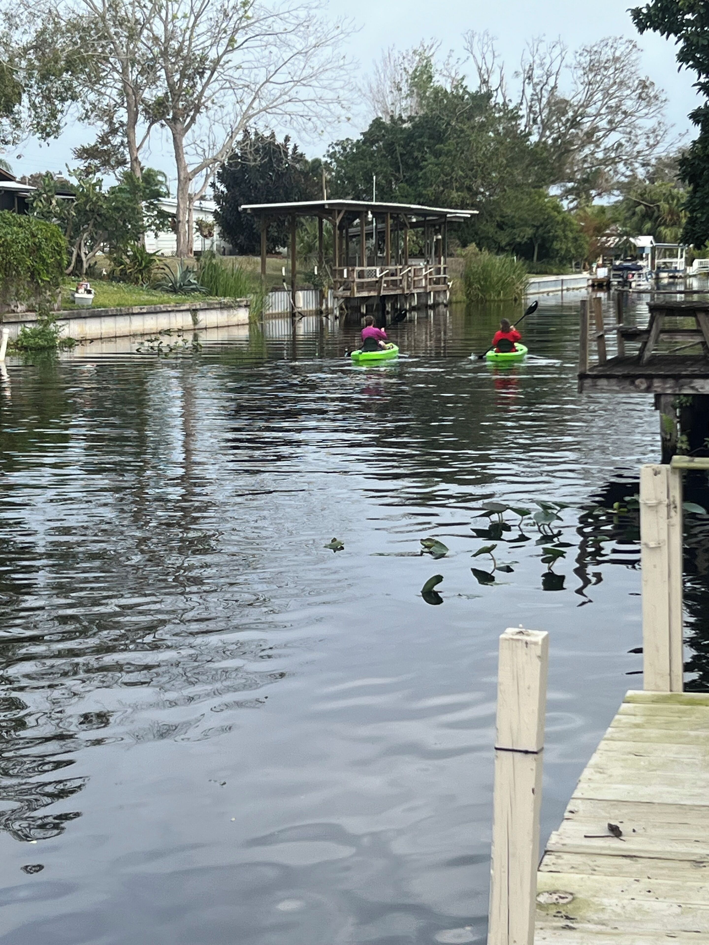 Un cuerpo de agua tranquilo con dos kayaks, un muelle de madera y un puente al fondo.