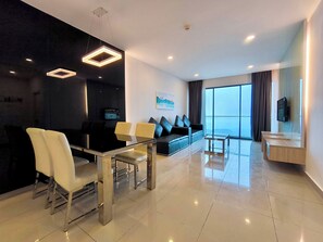 Una sala de estar moderna con un sofá negro, sillas blancas, una mesa de centro de vidrio y un televisor montado en la pared.