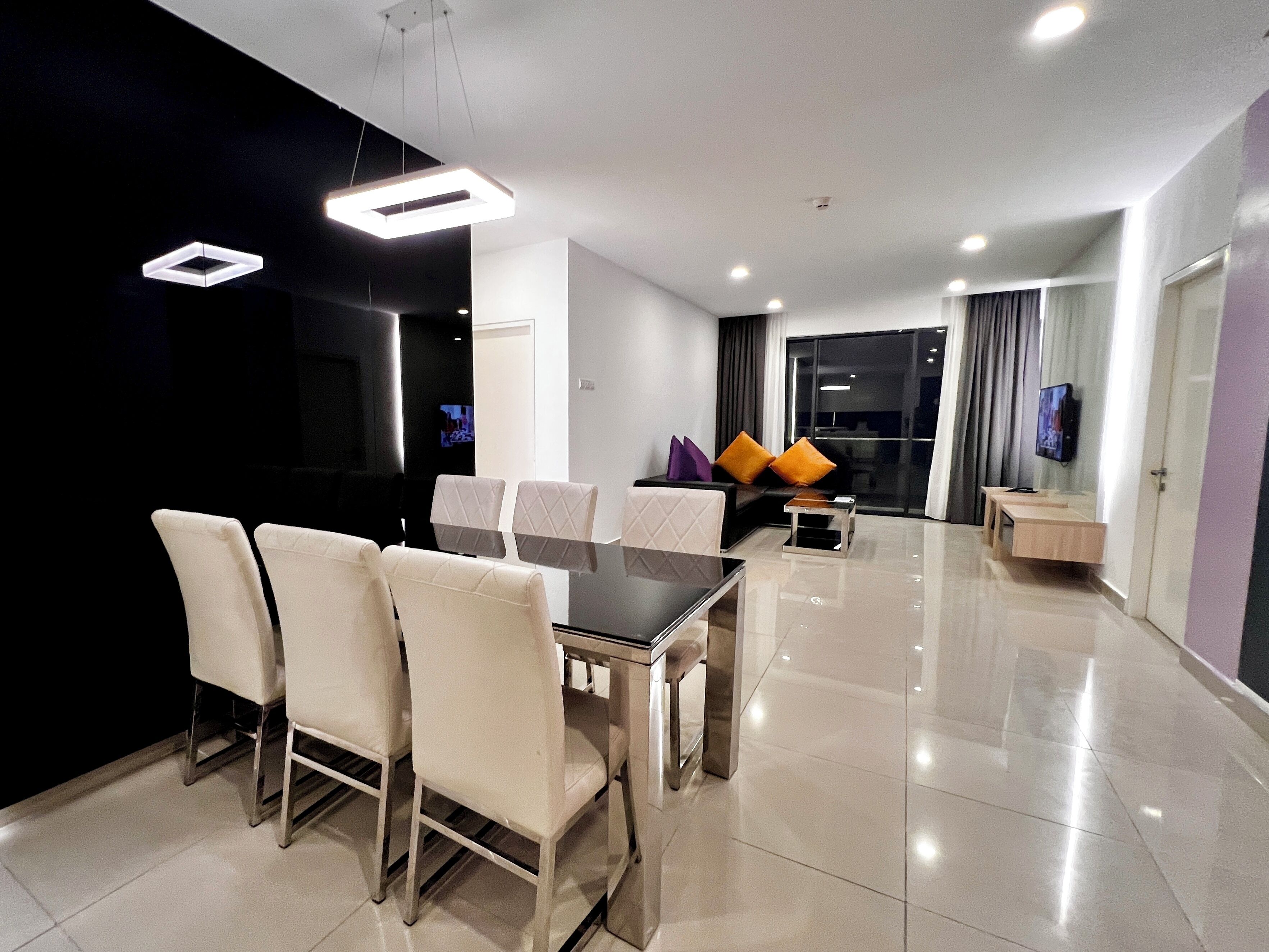 A modern dining area with a rectangular table and six chairs, a sofa with cushions, a small side table, and a television on the wall.