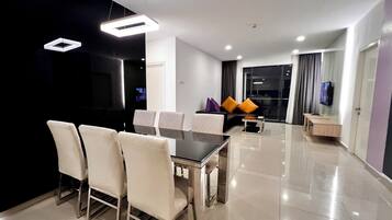 A modern dining area with a rectangular table and six chairs, a sofa with cushions, a small side table, and a television on the wall.