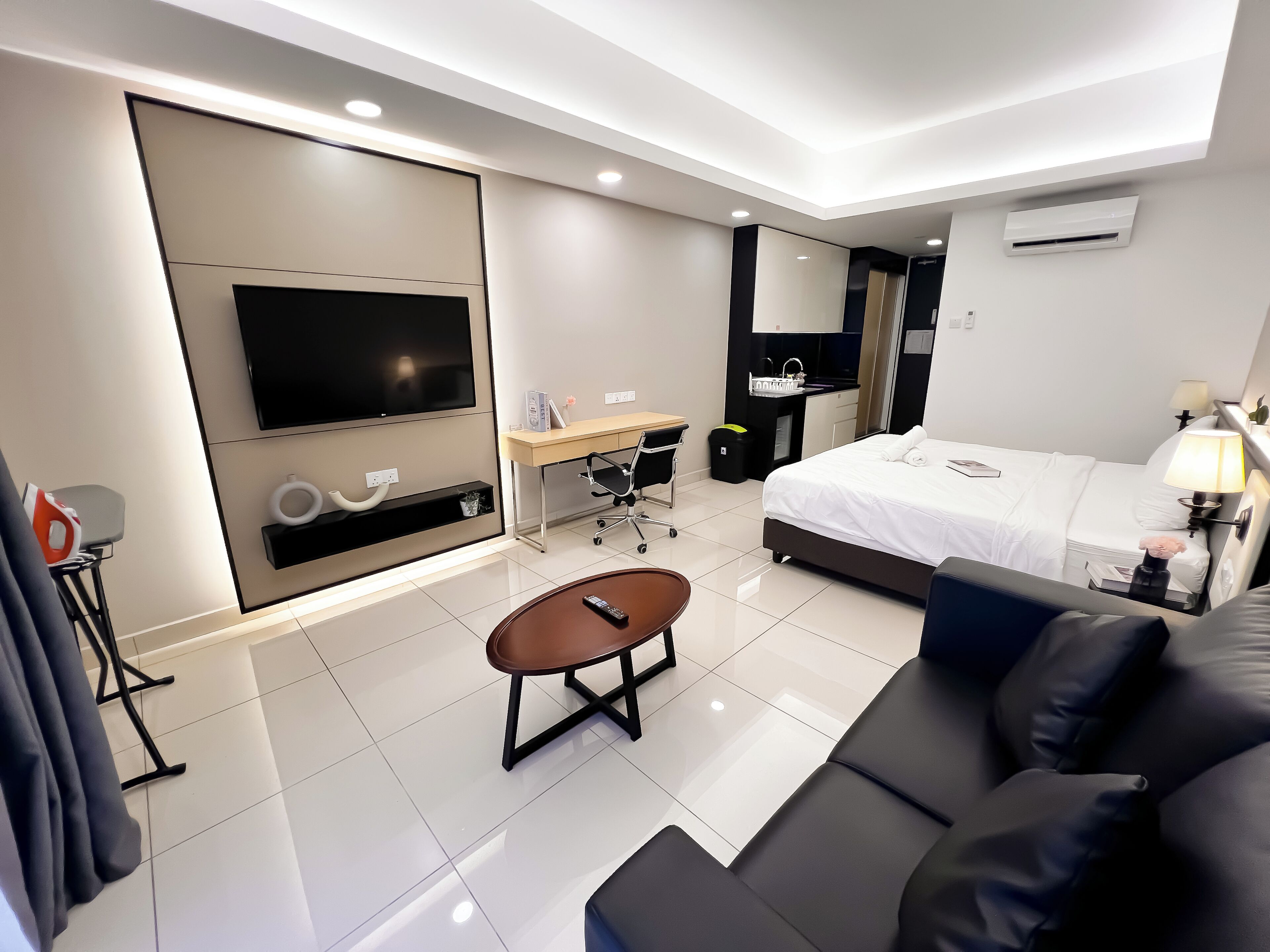 A modern hotel room with a large bed, a flat-screen TV, a desk with a chair, a small coffee table, and a sofa.