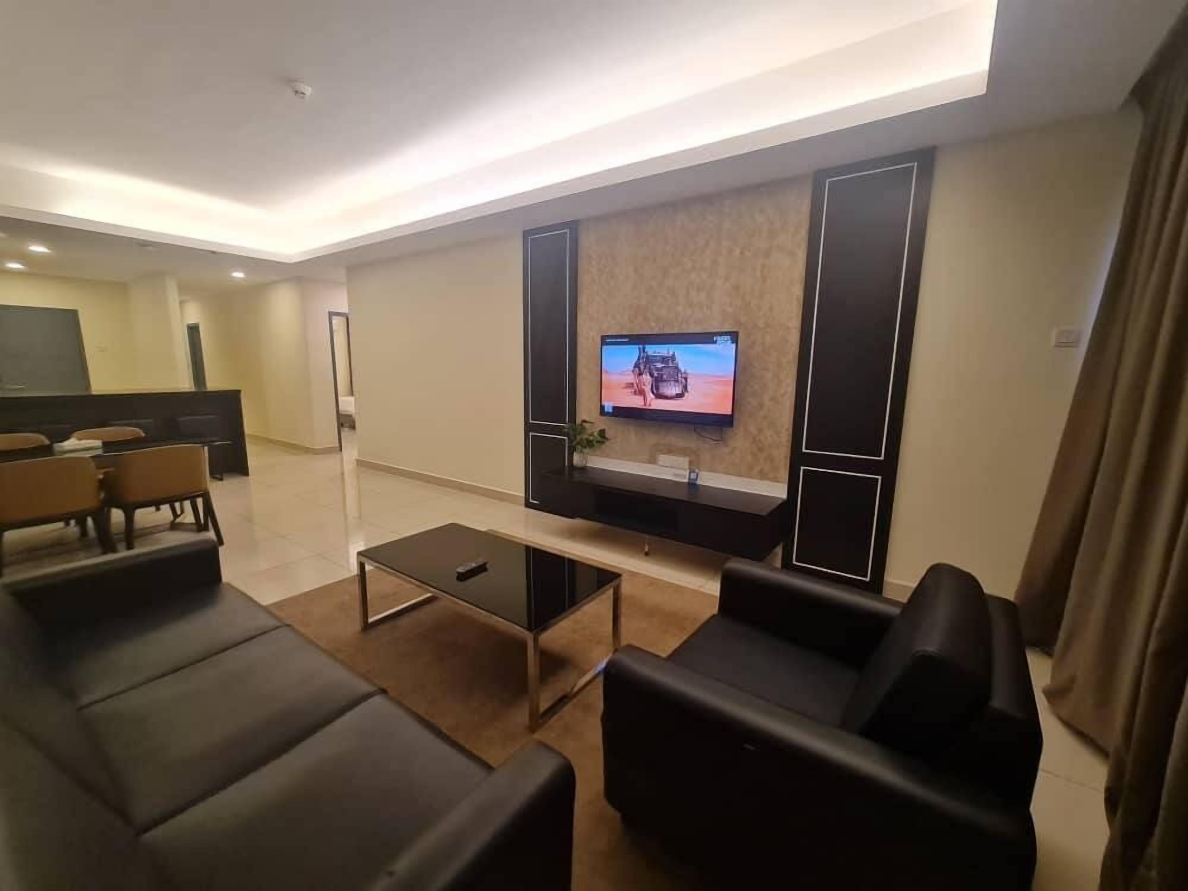Una sala de estar moderna con un televisor de pantalla plana montado en la pared, una mesa de centro y sofás de cuero negro.