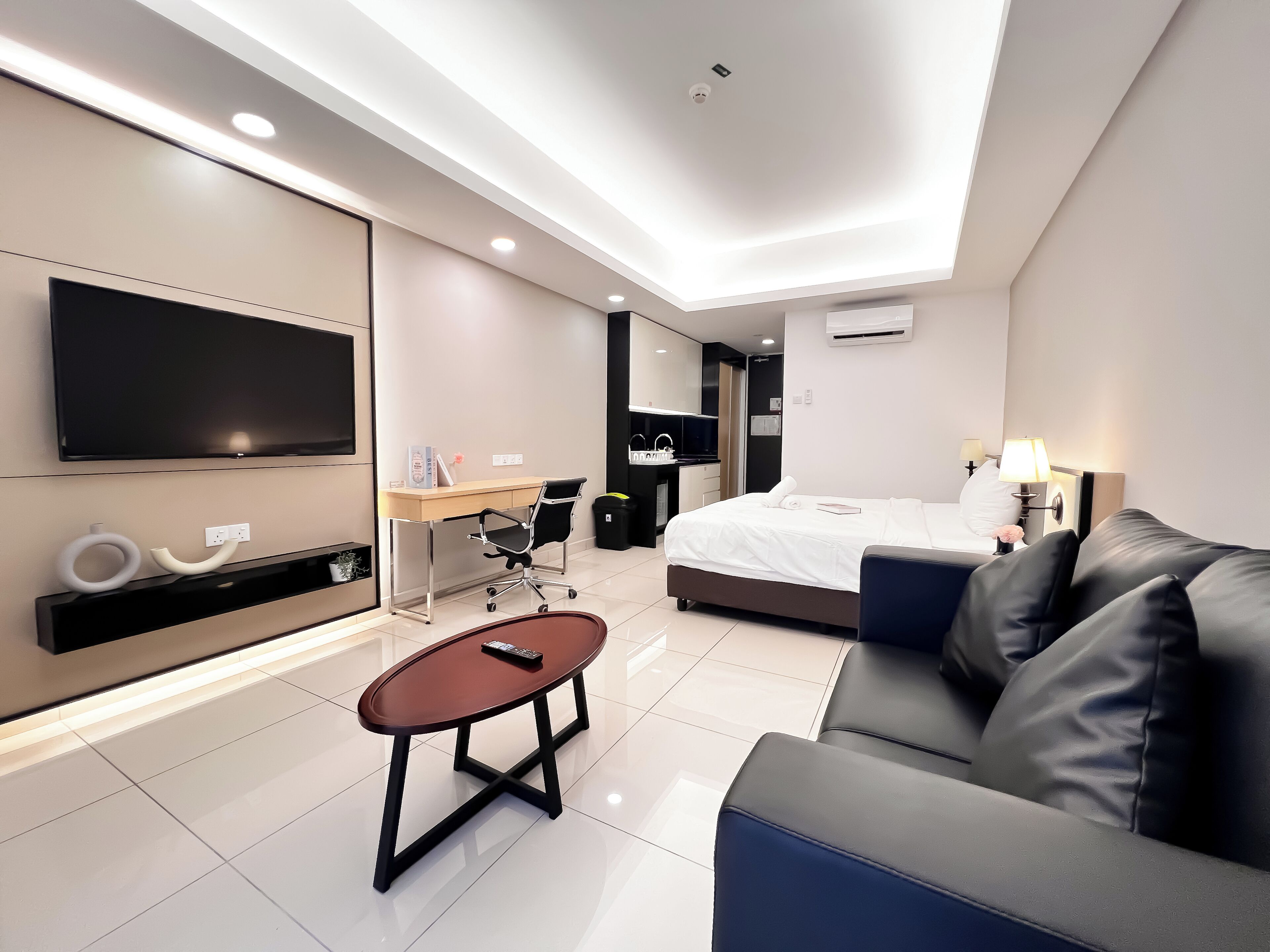 Et moderne hotelværelse med et stort fladskærms-tv, et skrivebord med stol, en seng med et natbord og en sofa.