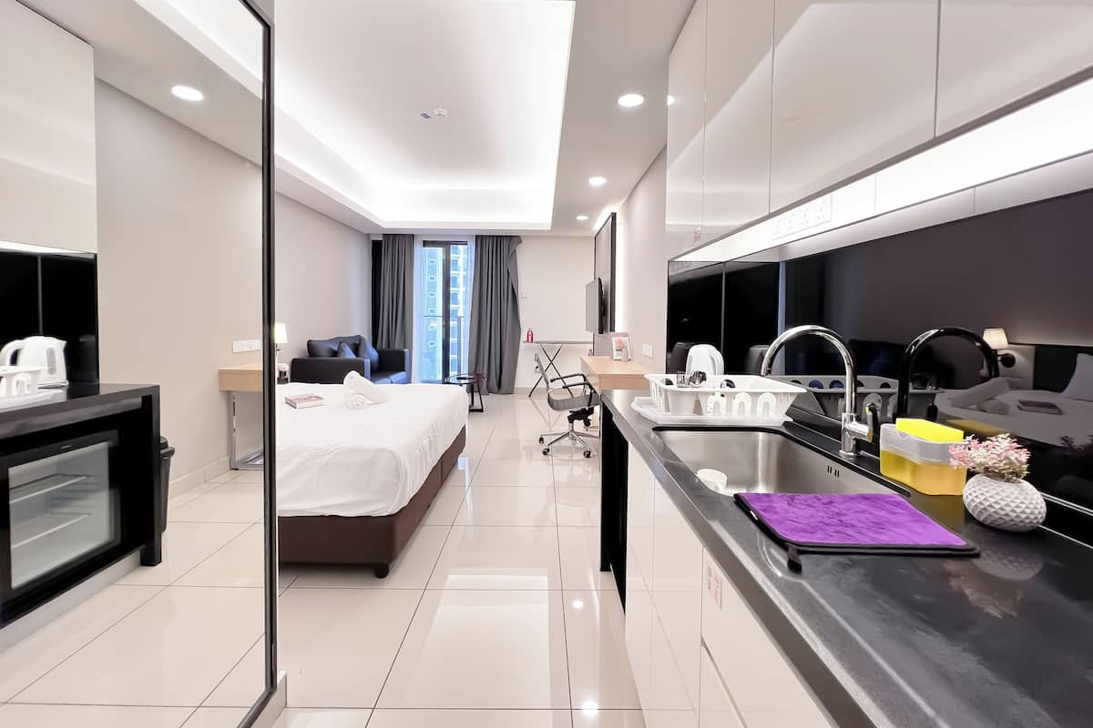 Habitación de hotel moderna con cama, escritorio, silla, televisor, baño con lavabo y espejo, y un ventanal grande.