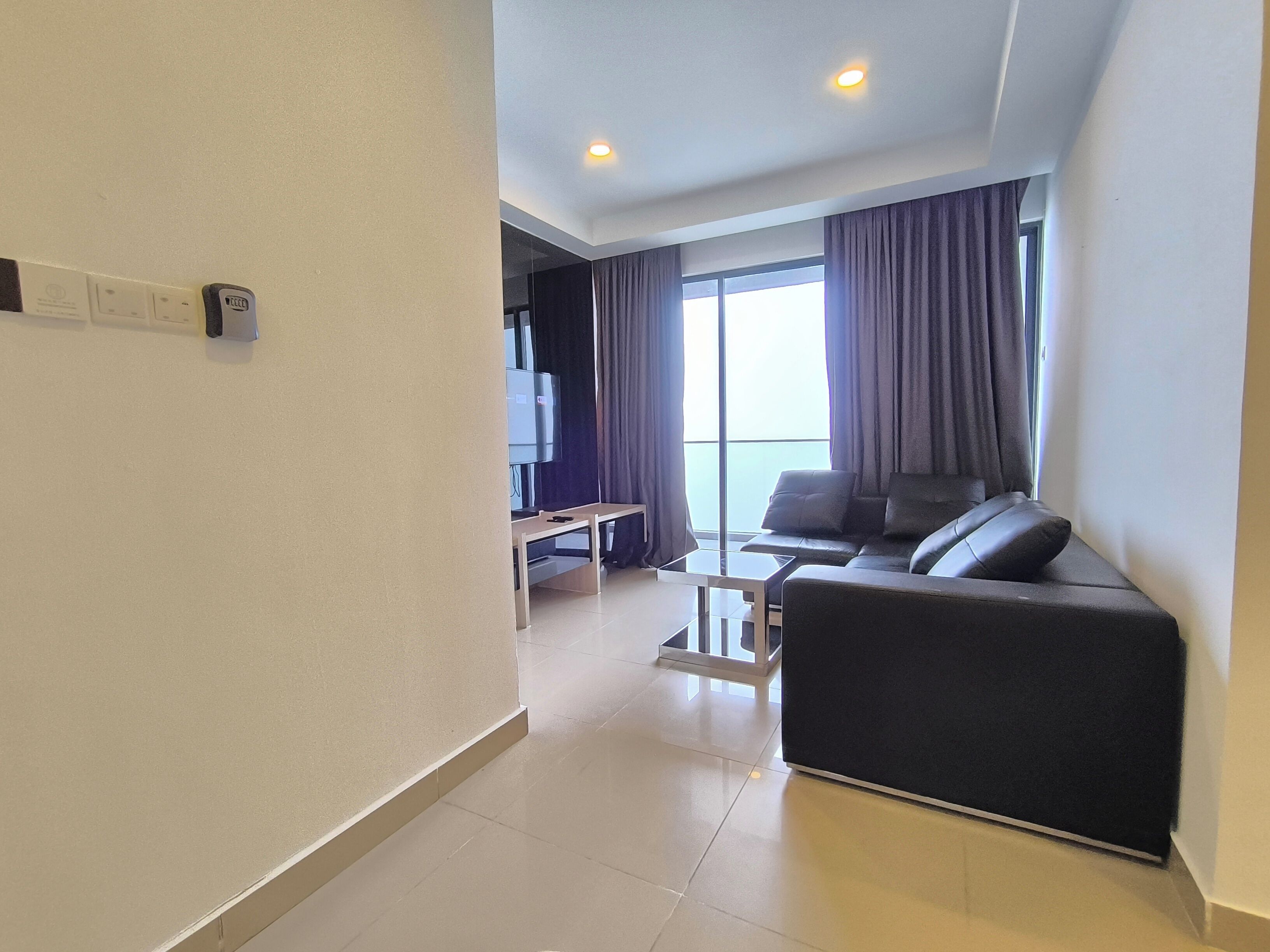 A modern living room with a sofa, a TV, and a balcony with curtains.