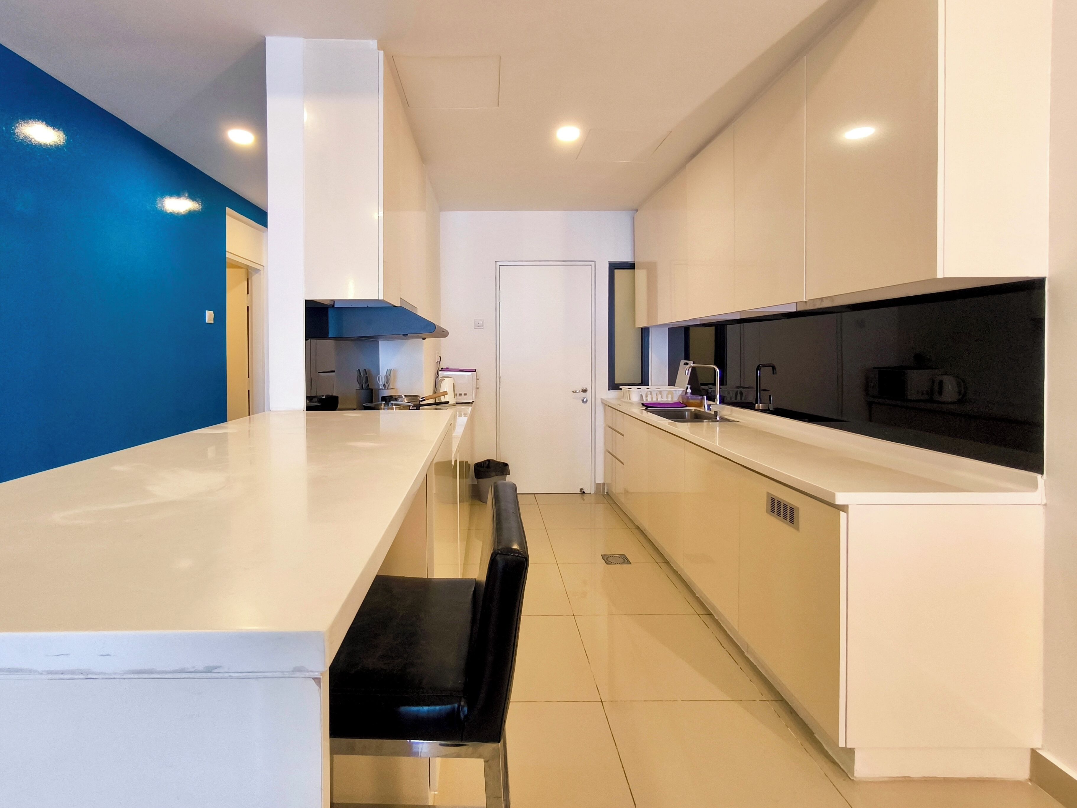 A modern kitchen with white cabinets, a black countertop, and a blue accent wall.