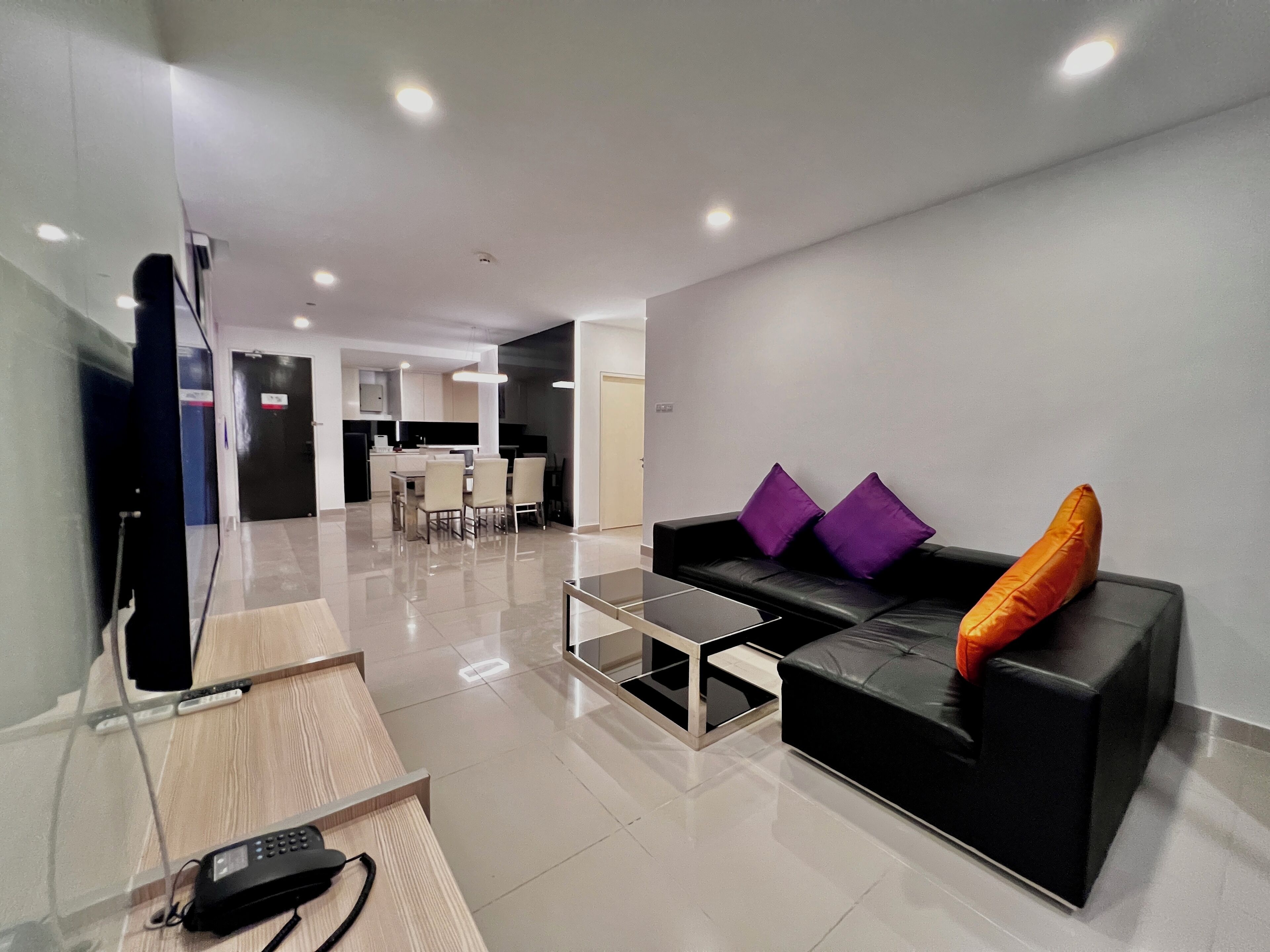 A modern living area with a black sofa, a coffee table, and a TV. There is a kitchen in the background.