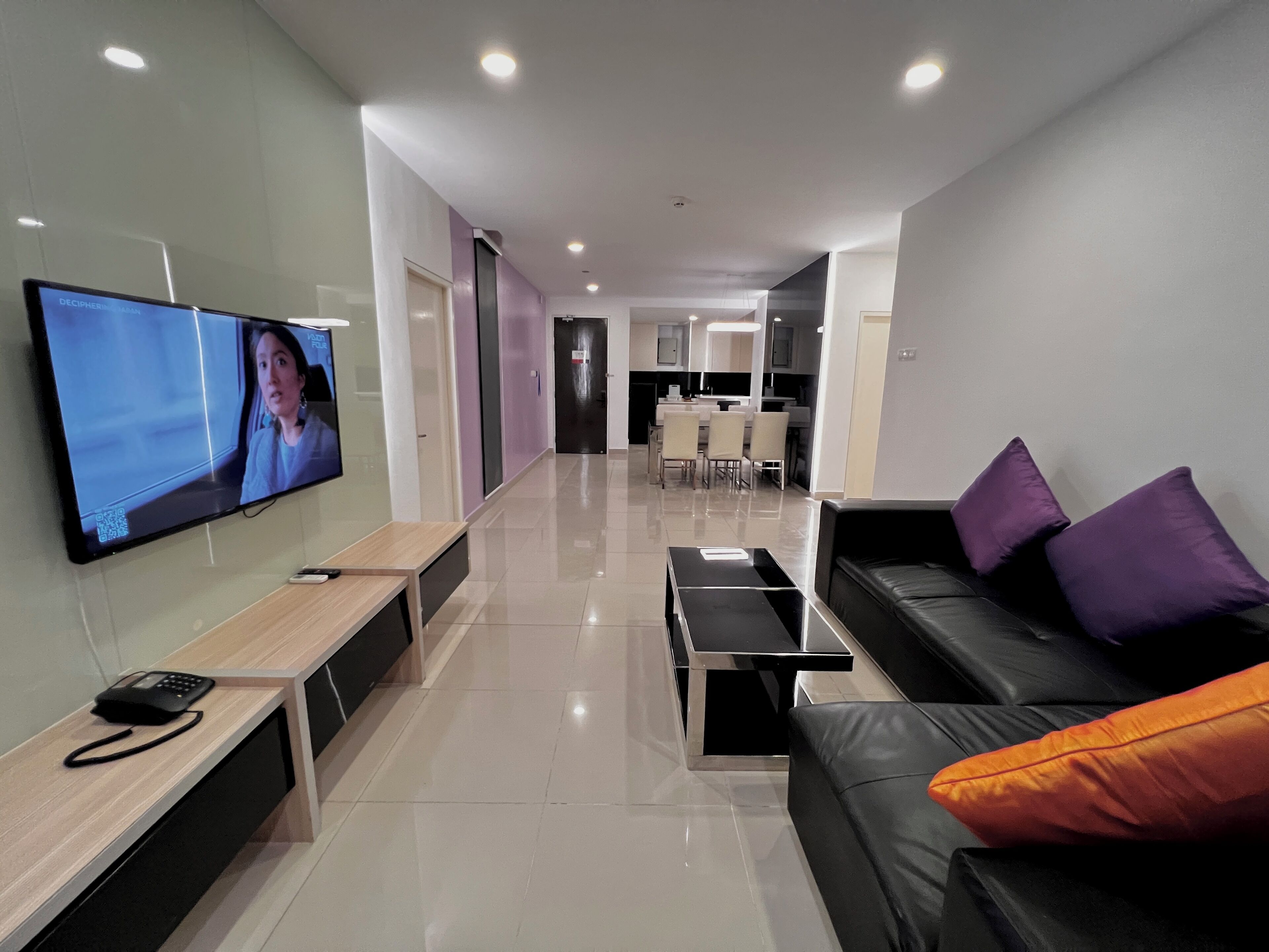A modern living room with a flat-screen TV, a sofa, a coffee table, and a dining area in the background.