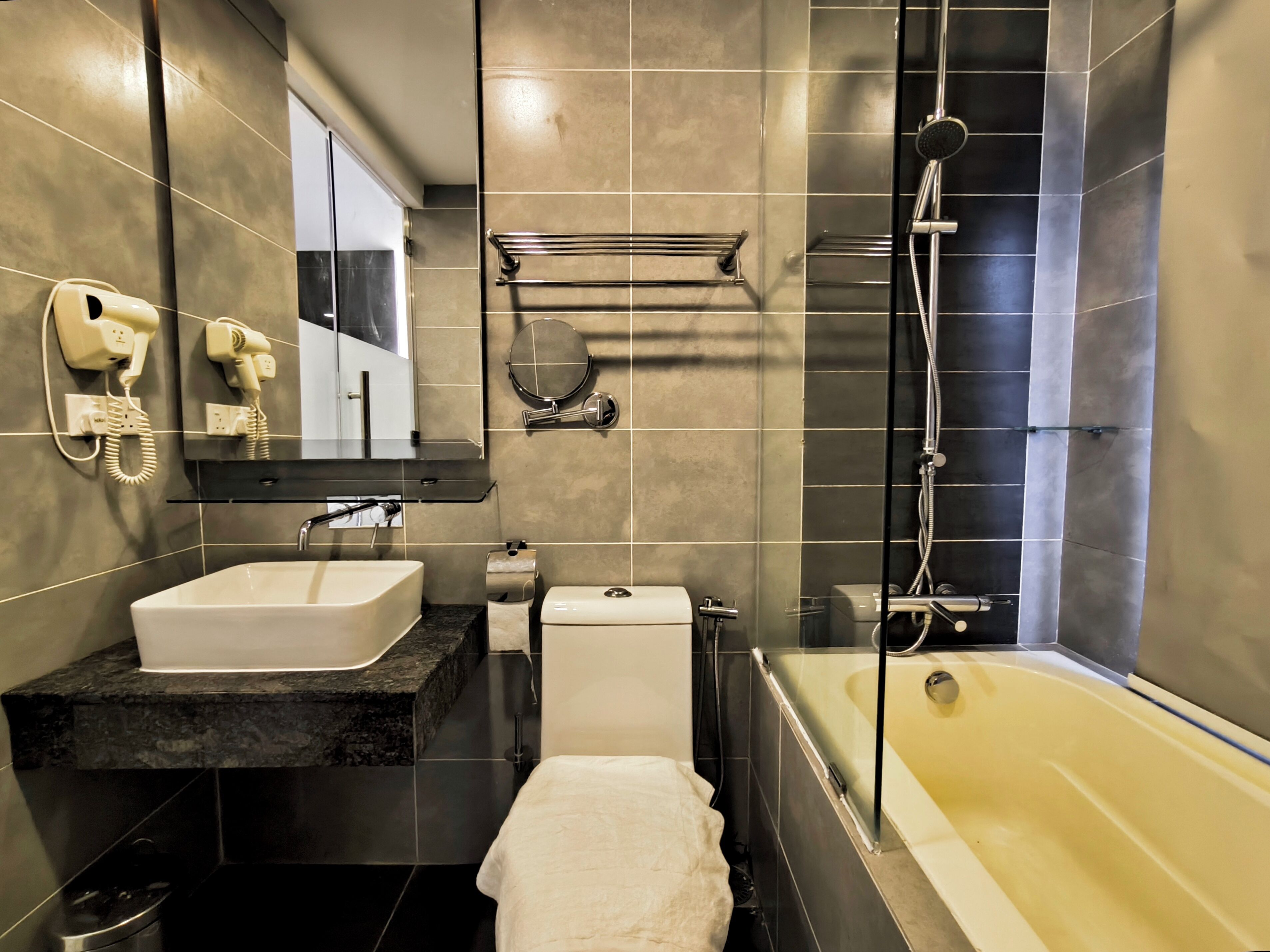 A modern bathroom with a bathtub, a sink, and a toilet. There are hair dryers mounted on the wall.
