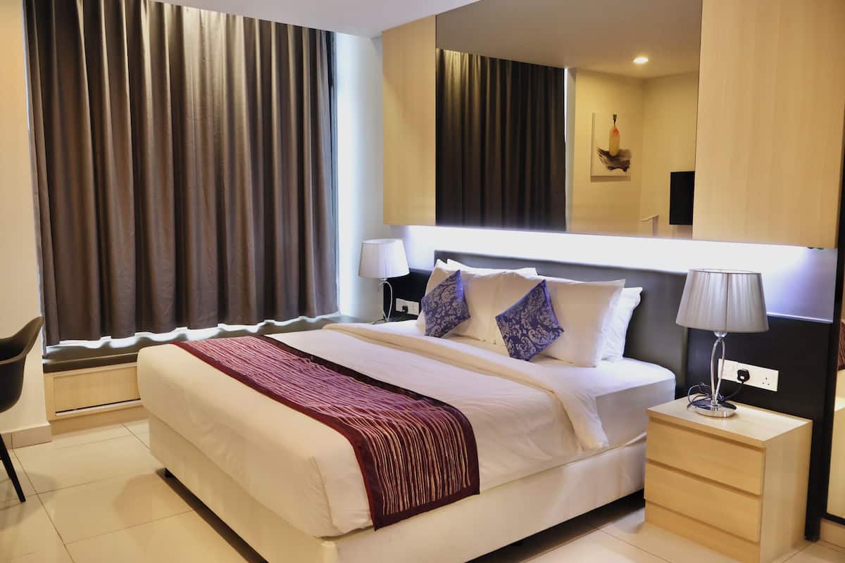 Habitación de hotel con una cama grande, dos mesitas de noche con lámparas, una silla y un ventanal con cortinas.