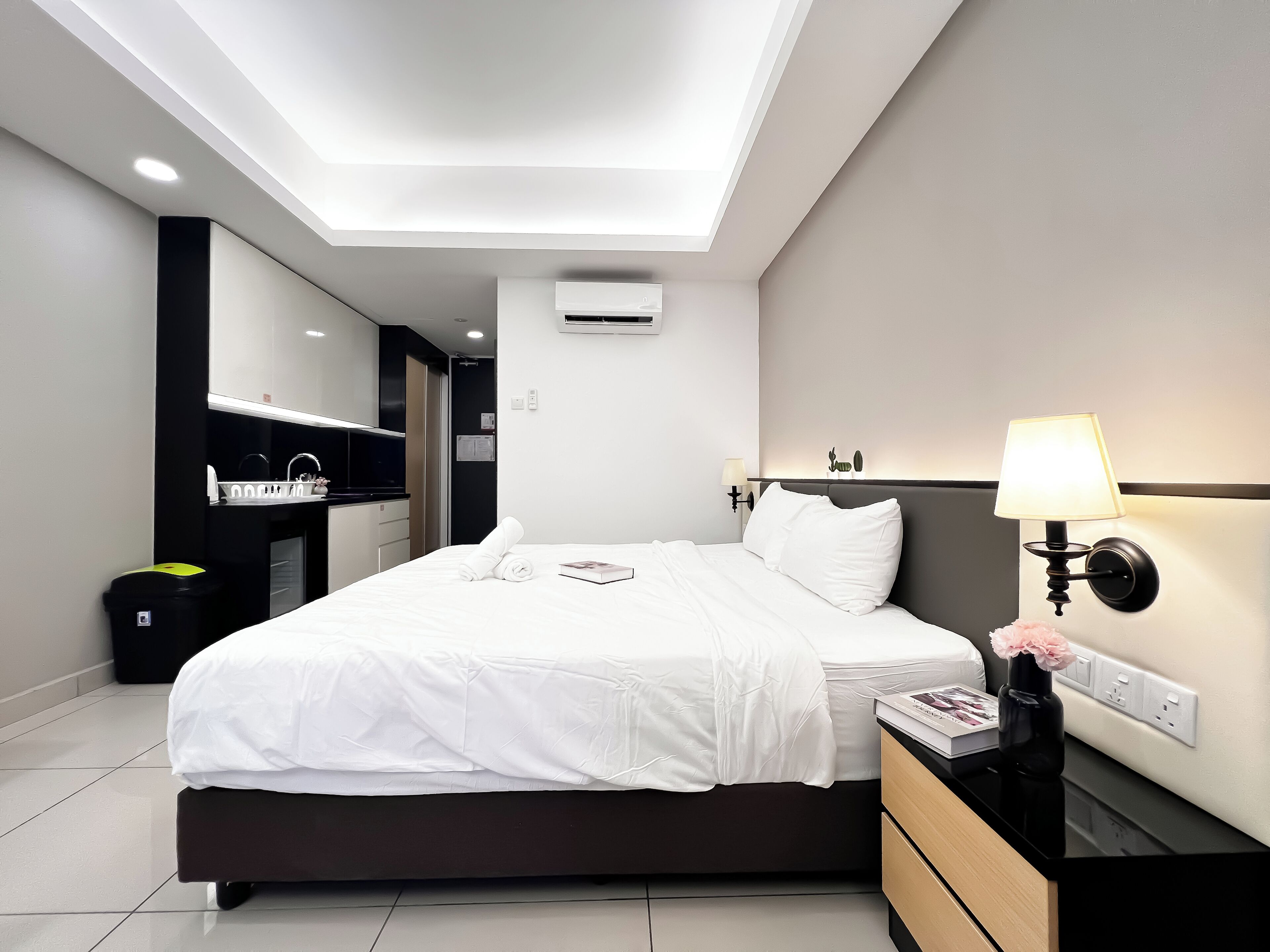 A modern hotel room with a neatly made bed, a bedside table with a lamp, and a small nightstand.