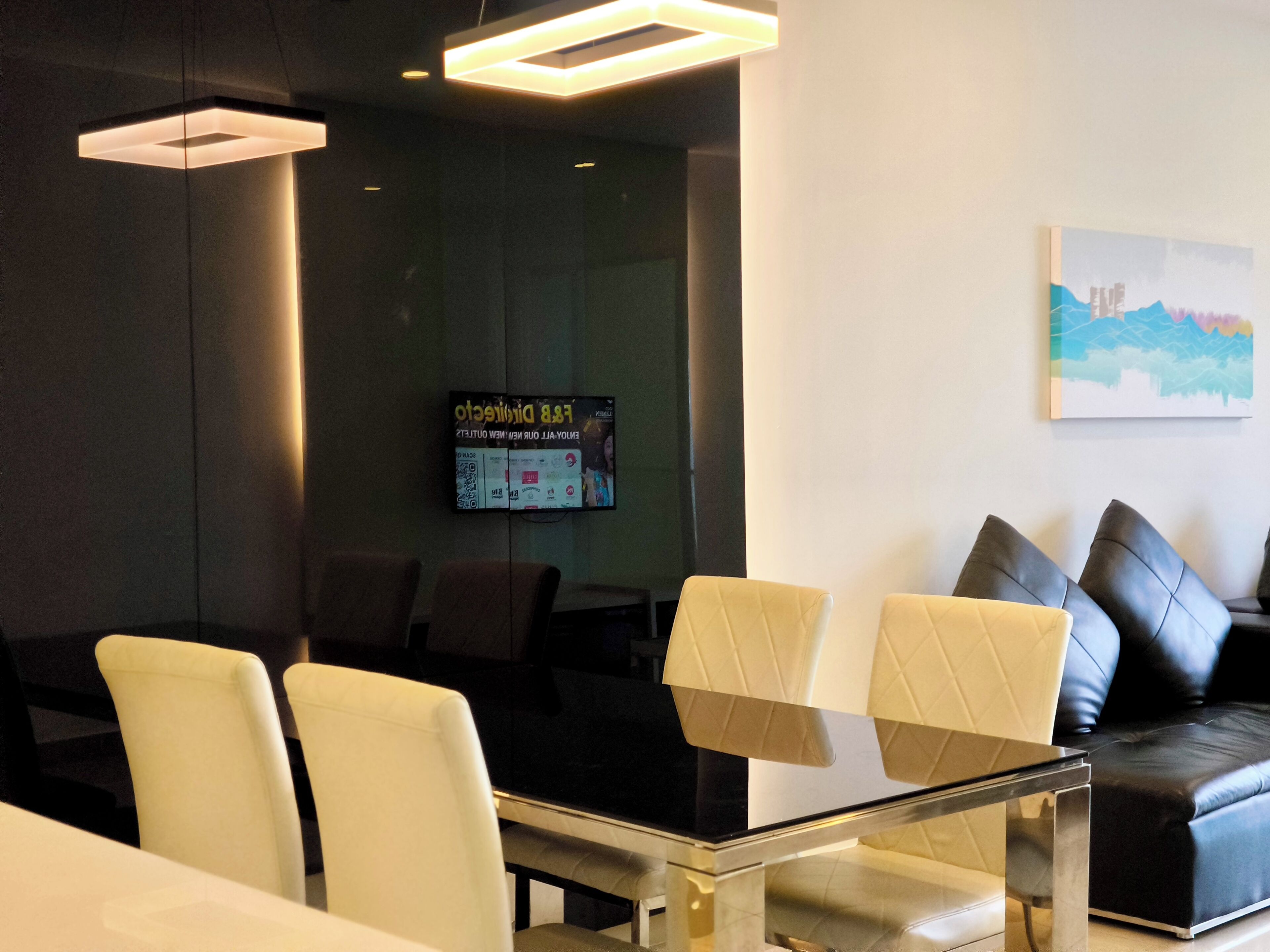 A modern waiting area with leather chairs, a glass table, and a mounted television displaying a promotional screen.