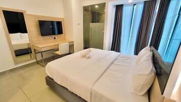 A modern hotel room with a large bed, a desk with a chair, a TV, and a bathroom with a glass door.