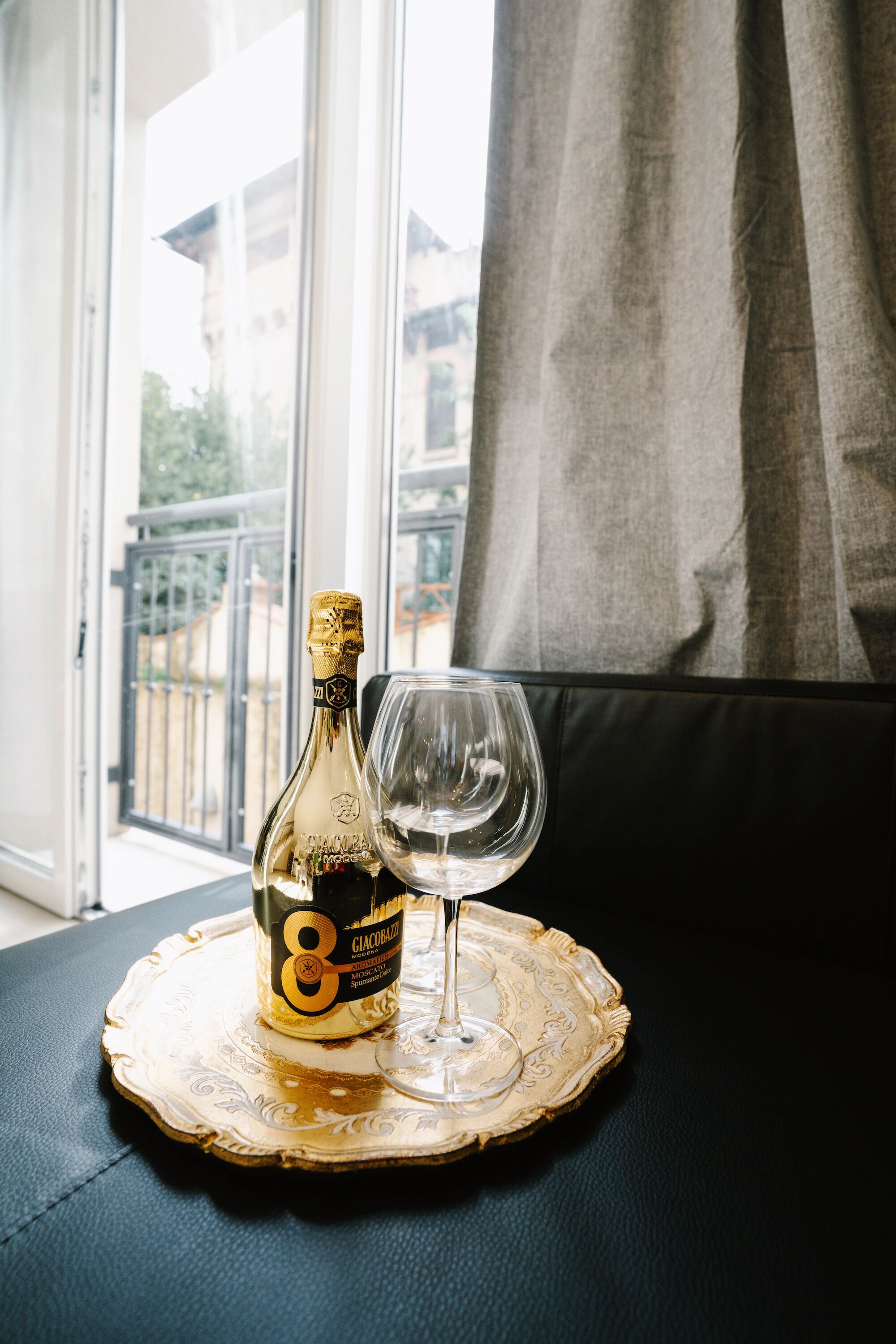 A bottle of Glace de Bourgogne on a decorative tray with a wine glass beside it, placed on a dark surface near a window with a view of buildings and a balcony.