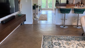 A modern kitchen with wooden cabinets, a stainless steel refrigerator, and a bar area with green bar stools. - Stay at GLORIA’S GETAWAY, a tranquil pastoral setting minutes from everything! (Winamac)