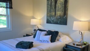A neatly arranged bedroom with a bed, two bedside tables, a ceiling fan, and a large forest-themed painting on the wall. - Stay at GLORIA’S GETAWAY, a tranquil pastoral setting minutes from everything! (Winamac)