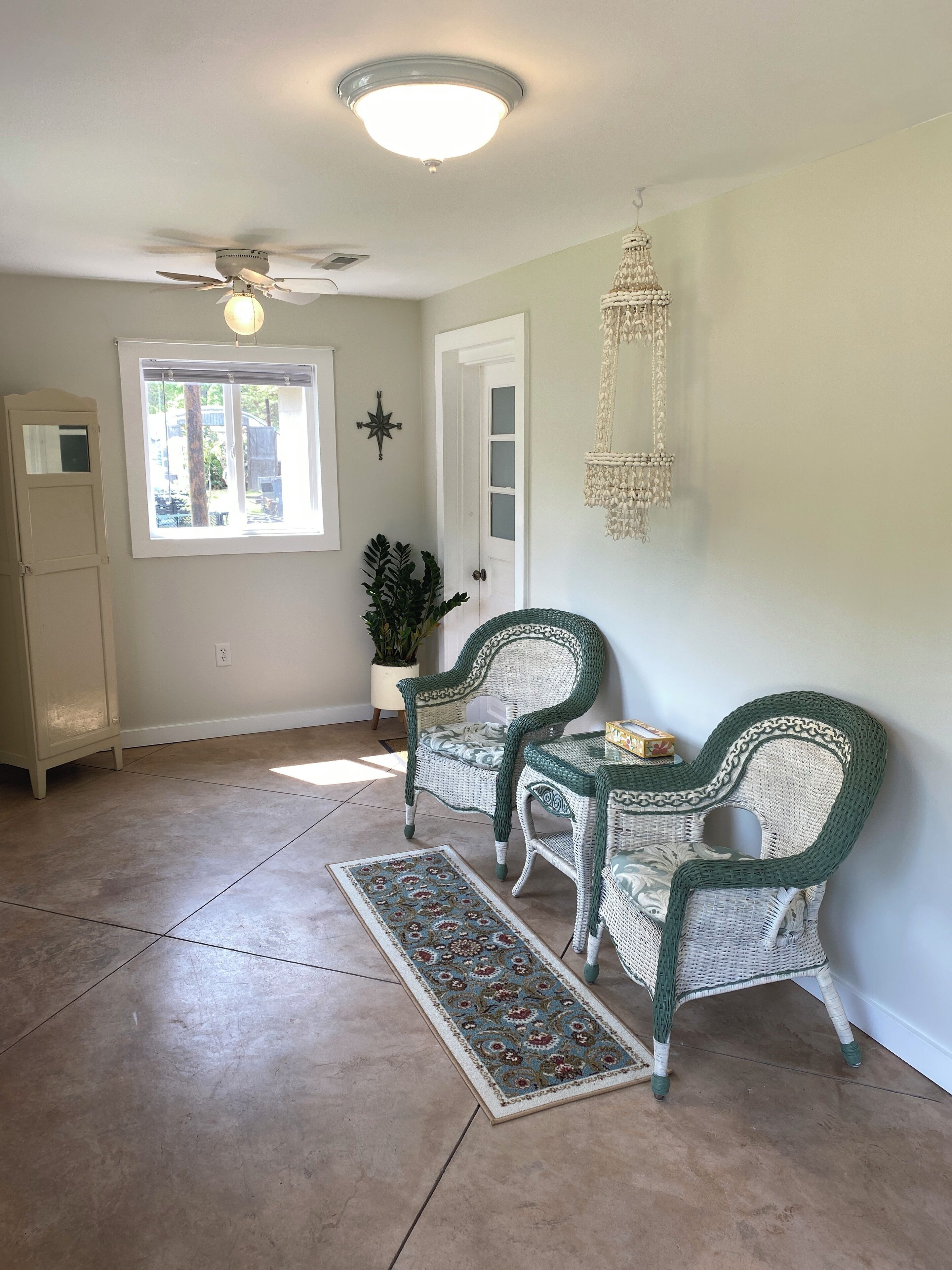 A spacious room with a ceiling fan, a large window, a decorative macrame hanging, and two wicker chairs.