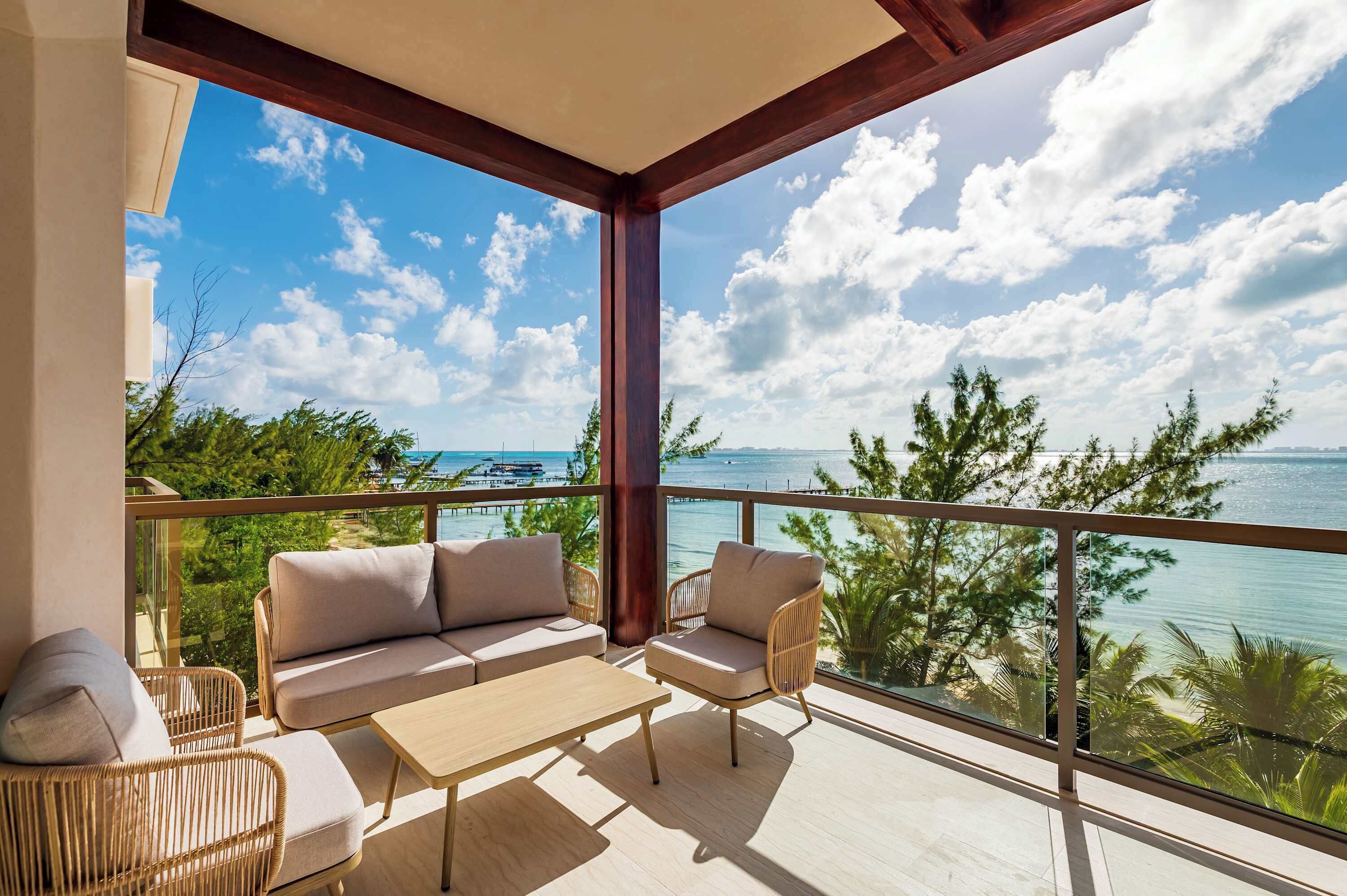A balcony with a sofa, chairs, and a table, overlooking a clear blue sky and a body of water.