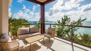 Un balcón con sofá, sillas y una mesa, con vista a un cielo azul despejado y una masa de agua.
