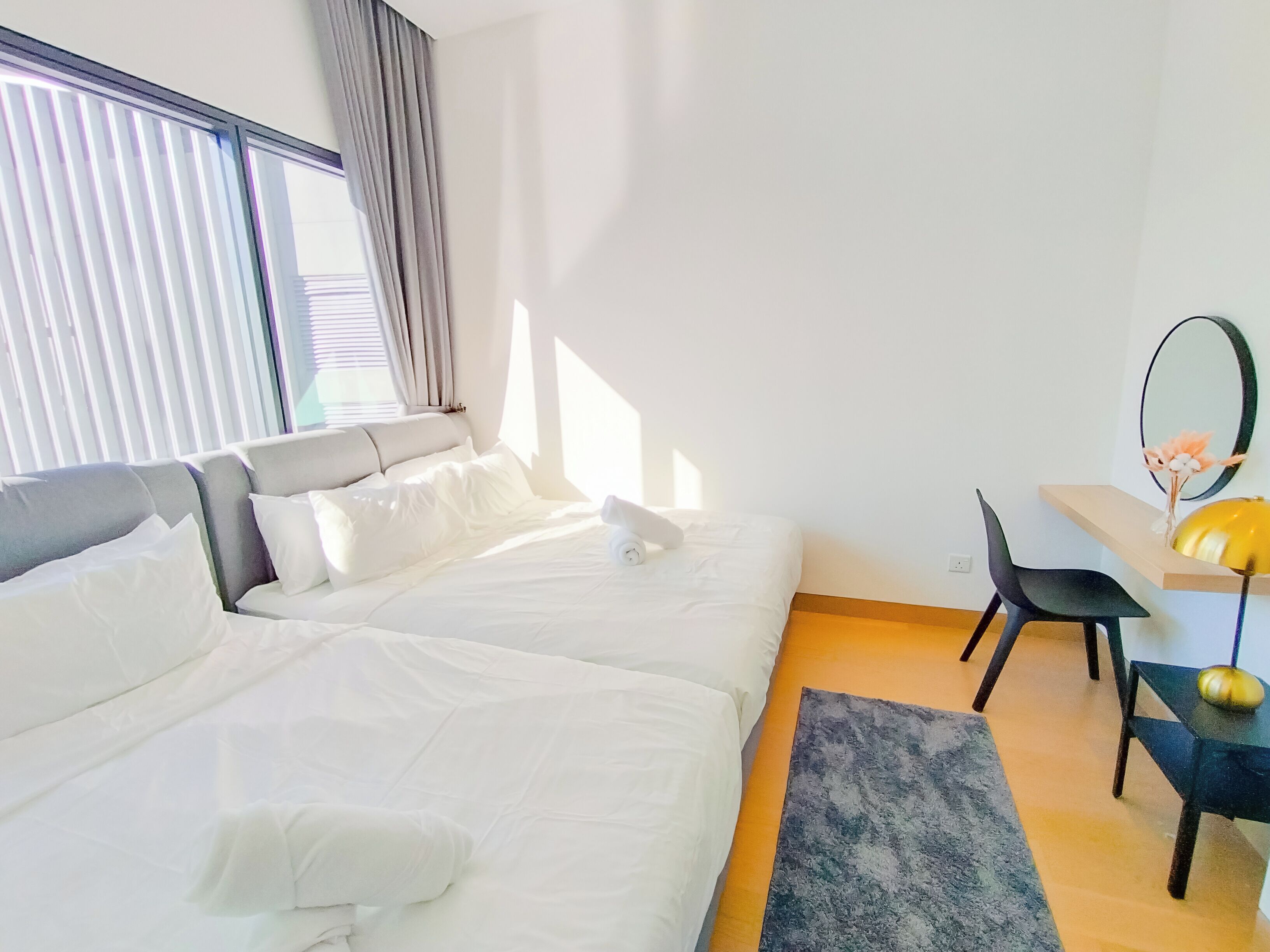 A modern hotel room with two beds, a desk, a chair, and a large window with blinds.