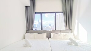 A hotel room with two beds, a large window with curtains, and a view of a cityscape.