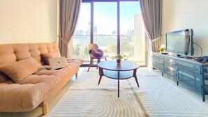 A modern living room with a sofa, a coffee table, a TV, and a view of the city through large windows.