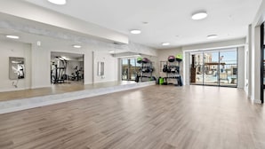 A spacious gym with wooden flooring, exercise equipment, and large windows offering views of the outside.