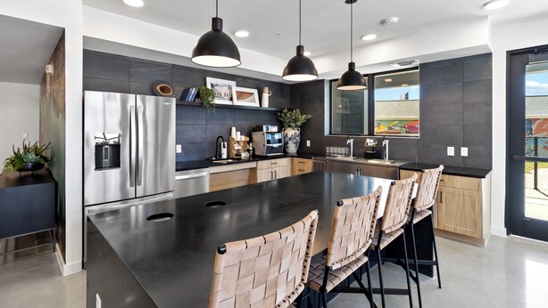 A modern kitchen with a large island, pendant lighting, stainless steel appliances, and a view to the outside.