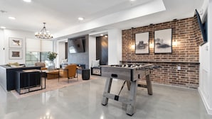 A spacious living area with a foosball table, a modern sofa, and a brick accent wall.