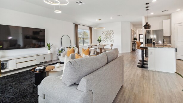 Een moderne woonkamer met een grijze bank, een flatscreen televisie en een eethoek met een tafel en stoelen.