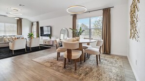 Een moderne woonkamer met een eethoek, met een ronde tafel, stoelen, een bank en een groot raam met gordijnen.