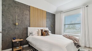 Een moderne slaapkamer met een groot bed, een nachtkastje, een klok aan de muur en een raam met gordijnen.