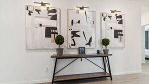 Een galerijwand met abstracte kunst, een klein tafeltje met een bord en twee potplanten.