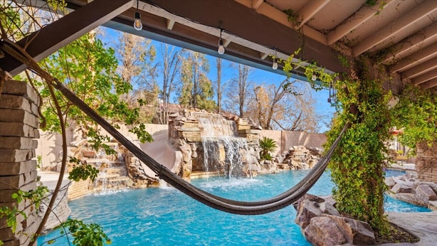 A hammock over a pool with a waterfall and rocky landscape.