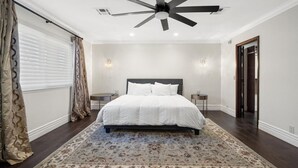 A bedroom with a large bed, a ceiling fan, two bedside tables, and a patterned rug.