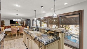 A kitchen with granite countertops, a dining area with patterned chairs, and a view of a swimming pool.